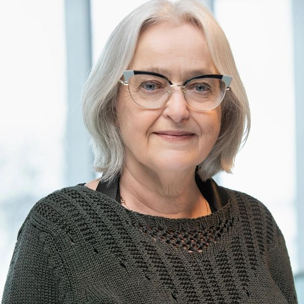 Smiling elderly woman with gray hair and glasses in a knitted sweater.
