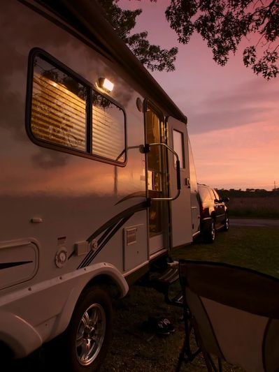 RV parked at sunset with warm light glowing inside and outdoor chair nearby.