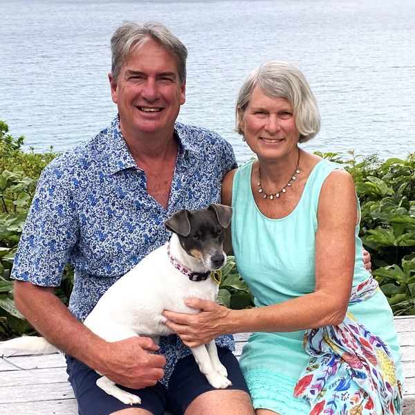 Happy couple sitting by the water with their dog.
