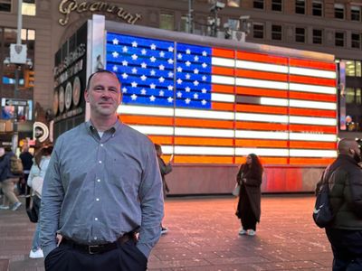 Man stands smiling in front of a large illuminated American flag display.