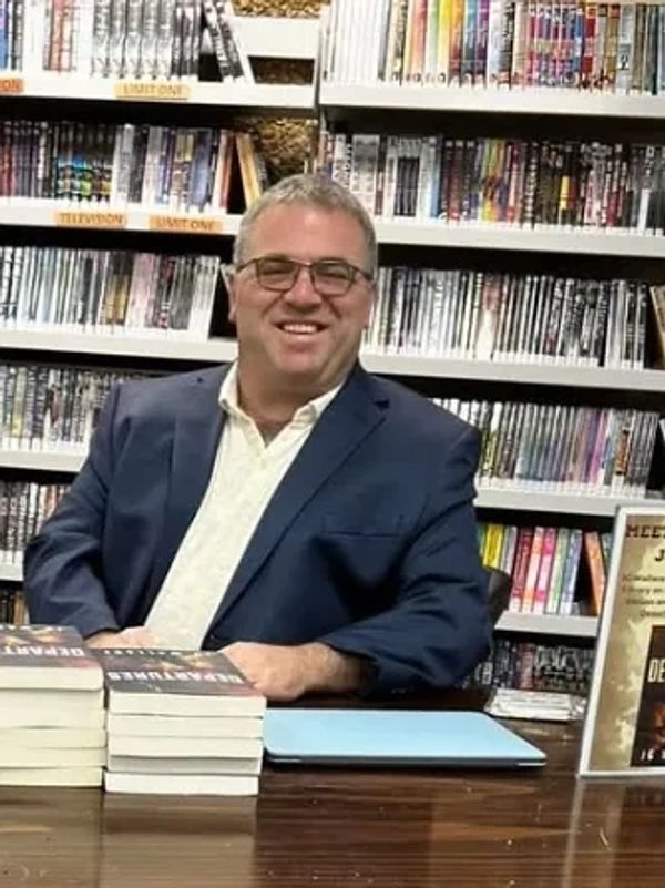 JG Wallace sitting at a desk at a library with copies of Departures in front of him.