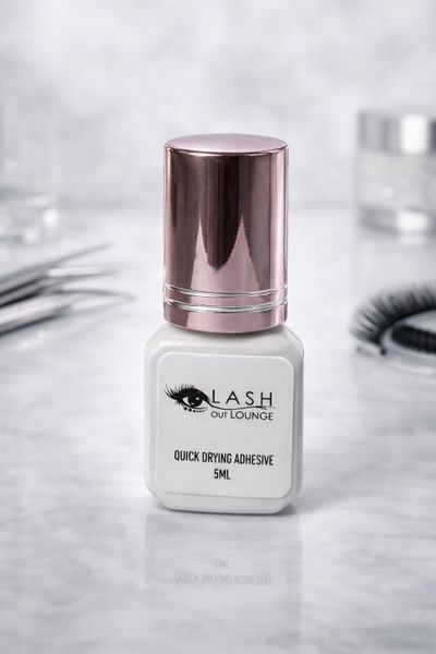 Quick drying eyelash adhesive bottle with a rose gold cap on a marble surface.