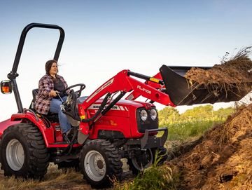 Woman operating red Massey Ferguson tractor with front loader on farmland.