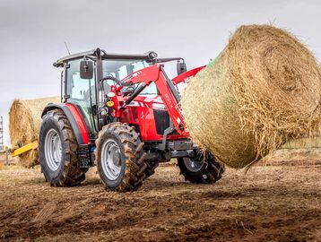 Red tractor carrying large round hay bales in a field.
