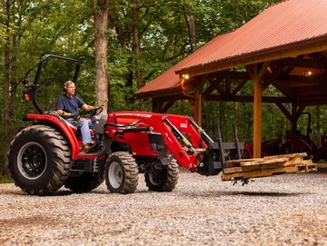 Man driving a red tractor with wooden pallets in a wooded area.