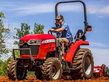 Person operating a red Massey Ferguson tractor on a farm field.