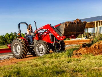A woman operating a red tractor with a front loader full of dirt.