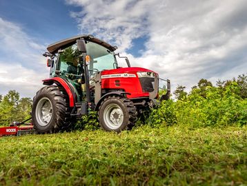 Red Massey Ferguson tractor in a green field under a cloudy sky.