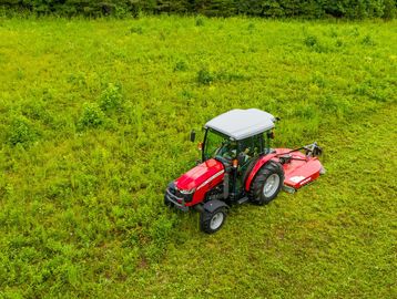 Red tractor mowing a lush green field with dense vegetation.
