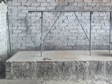 An unfinished concrete platform with metal railings and a bucket in a rustic brick room.