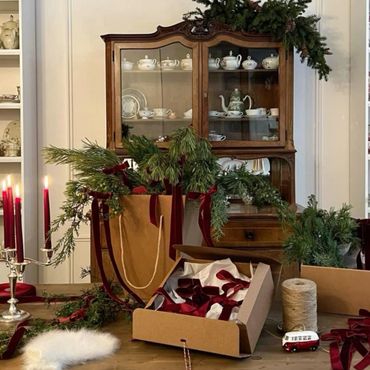A cozy holiday scene with greenery, candles, and gift wrapping supplies on a wooden table.
