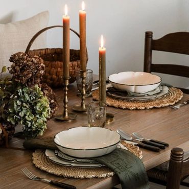 Rustic dining table set with candles, woven placemats, and vintage dishware.
