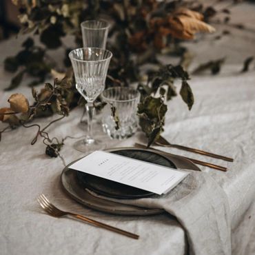 Elegant table setting with dried foliage, crystal glasses, and minimalist menu on rustic plates.