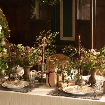Elegant holiday table setting with candles, greenery, and wrapped gifts.