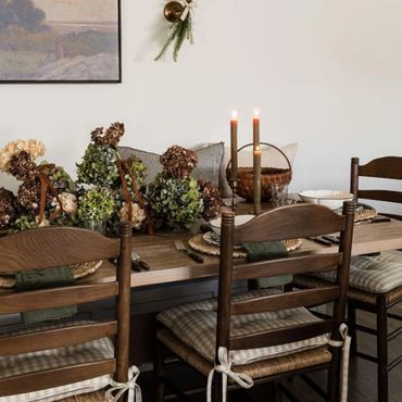 Rustic dining table with wooden chairs, candles, and dried floral centerpiece.