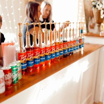 Row of flavored syrups and soda cans on a counter.