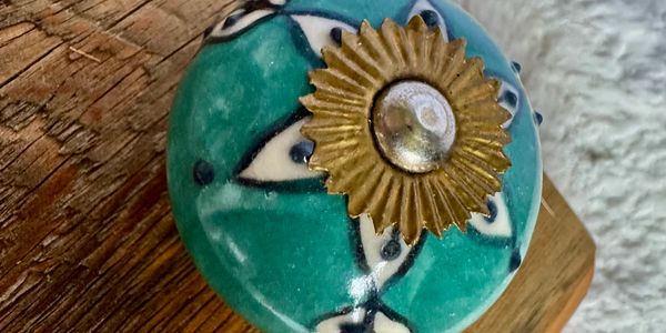 Decorative teal ceramic knob with brass sunburst center on wooden surface.