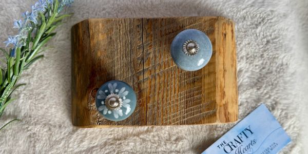 Decorative wooden board with two blue ceramic knobs and a business card on plush fabric.