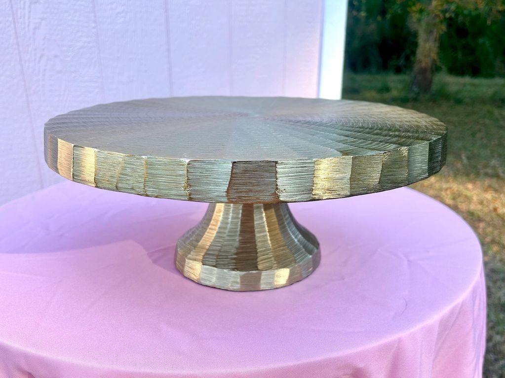 Metallic cake stand with a textured, brushed finish on a pink tablecloth.
