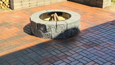 A stone fire pit with wood logs on a brick patio.