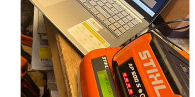 STIHL AP 500 S battery charging on an orange charger next to a laptop.