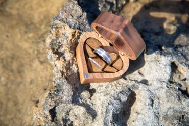 Two rings in a wooden heart-shaped box on a rock.