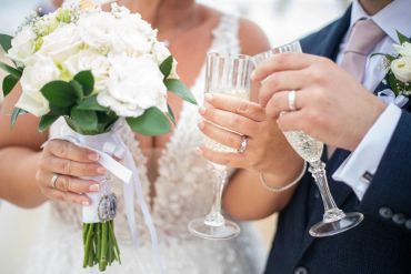 Newlyweds toasting with champagne and holding a bouquet.