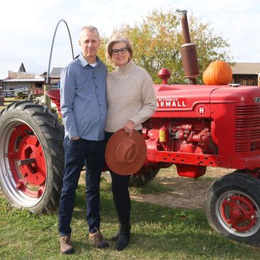 Couple standing by a red vintage tractor holding a hat outdoors.