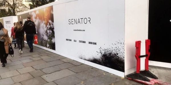 Pedestrians walking past a construction site with Senator branding on the hoarding.