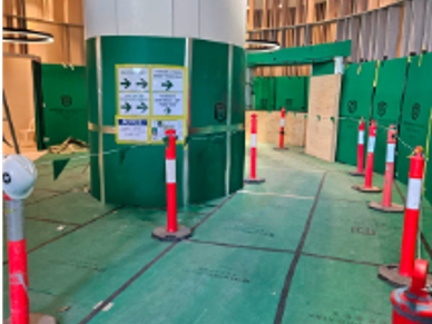 Indoor construction area with green protective barriers and orange safety cones.