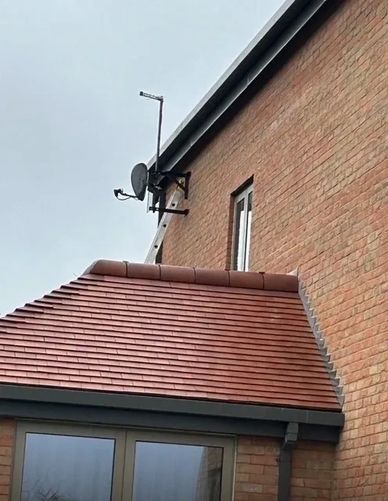 A cat climbing on a satellite dish attached to a brick house.
