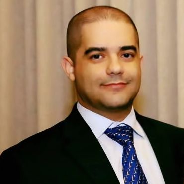 Man in suit with blue patterned tie smiling gently.