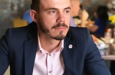 Man in a suit sitting thoughtfully at a table in a restaurant.