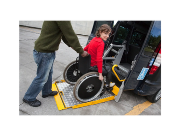 Woman being helped into a wheelchair taxi