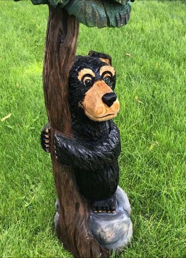 Carved wooden bear hugging a tree on green grass.