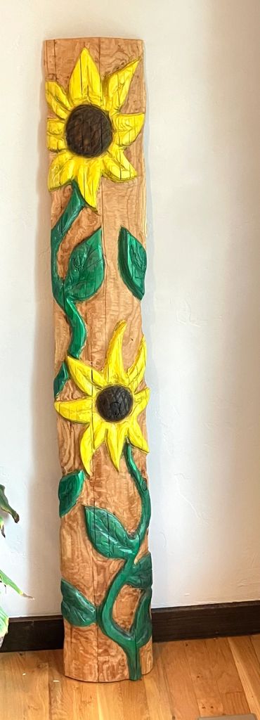 Wooden sunflower carving with bright yellow petals and green leaves.