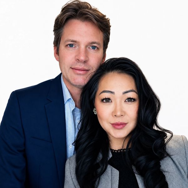 A man and woman pose closely, dressed in formal attire against a white background.