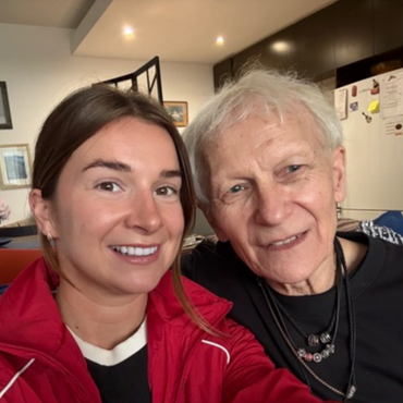 A young woman and an elderly man smiling together for a selfie indoors.