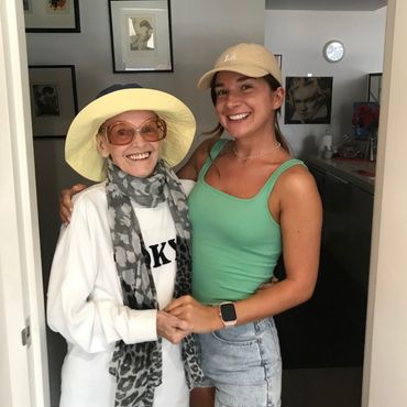 Two women smiling and posing together indoors, wearing hats and casual clothes.