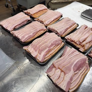 Multiple trays of raw bacon slices arranged on a metal countertop.