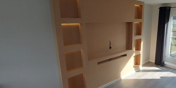 Modern beige wall unit with built-in shelves and ambient lighting in a bright room.