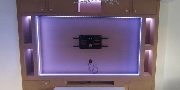 Modern TV wall mount setup with ambient purple LED lighting and wooden cabinetry.