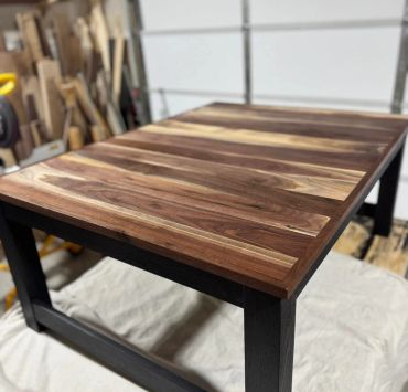 Wooden dining table with dark legs and a striped natural wood top.