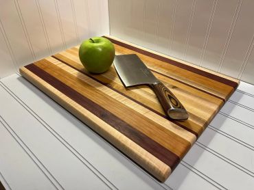 A green apple and knife on a striped wooden cutting board.