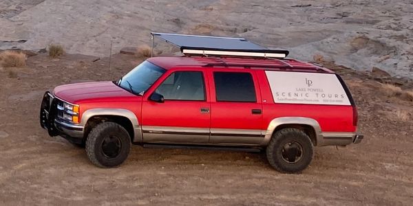 Lake Powell Scenic Tour's red suburban tour vehicle parked at Stud Horse Point at sunset