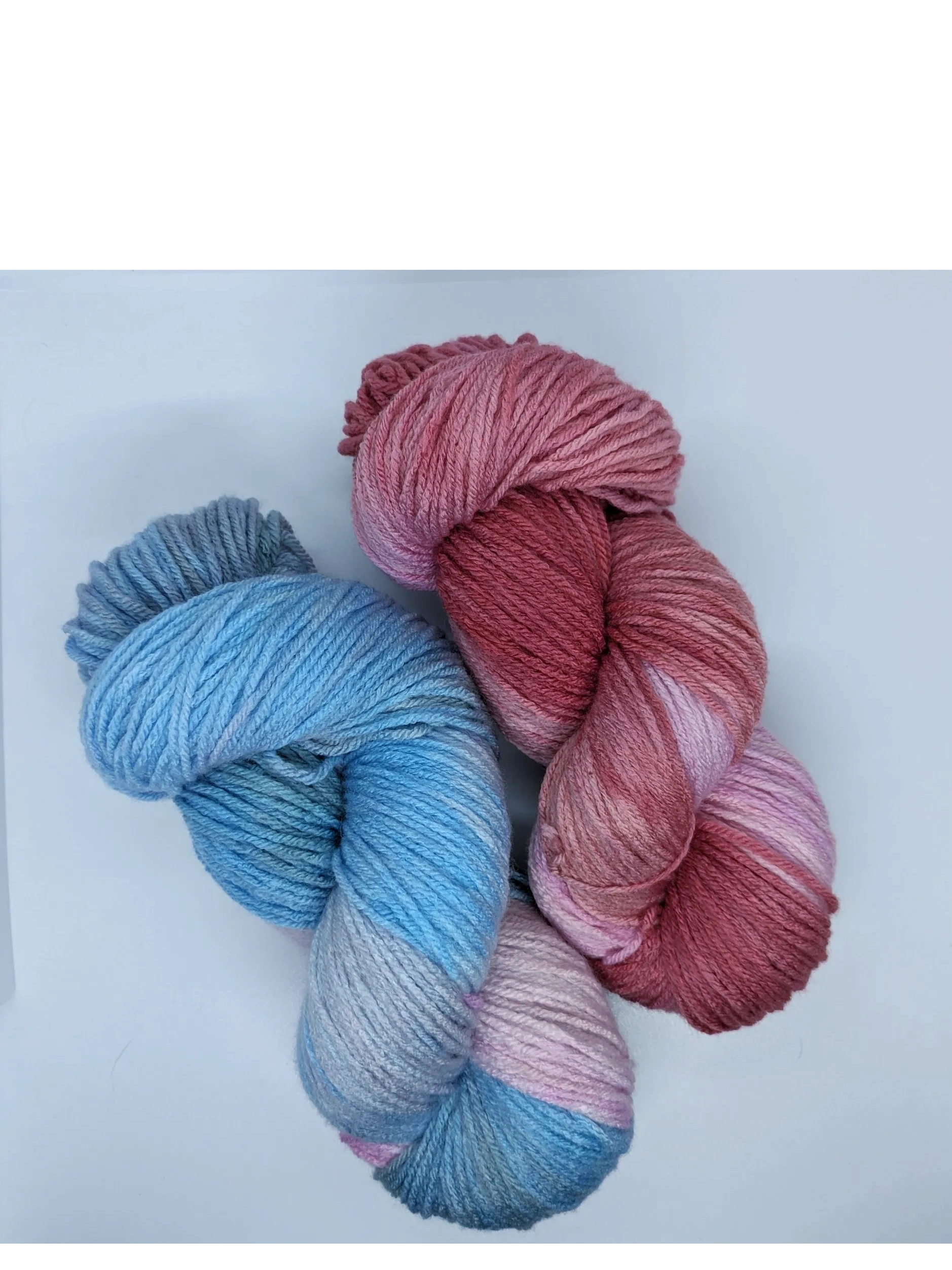 2 twisted skeins of yarn on a white background. One is light blue & pink, the other is red & pink.