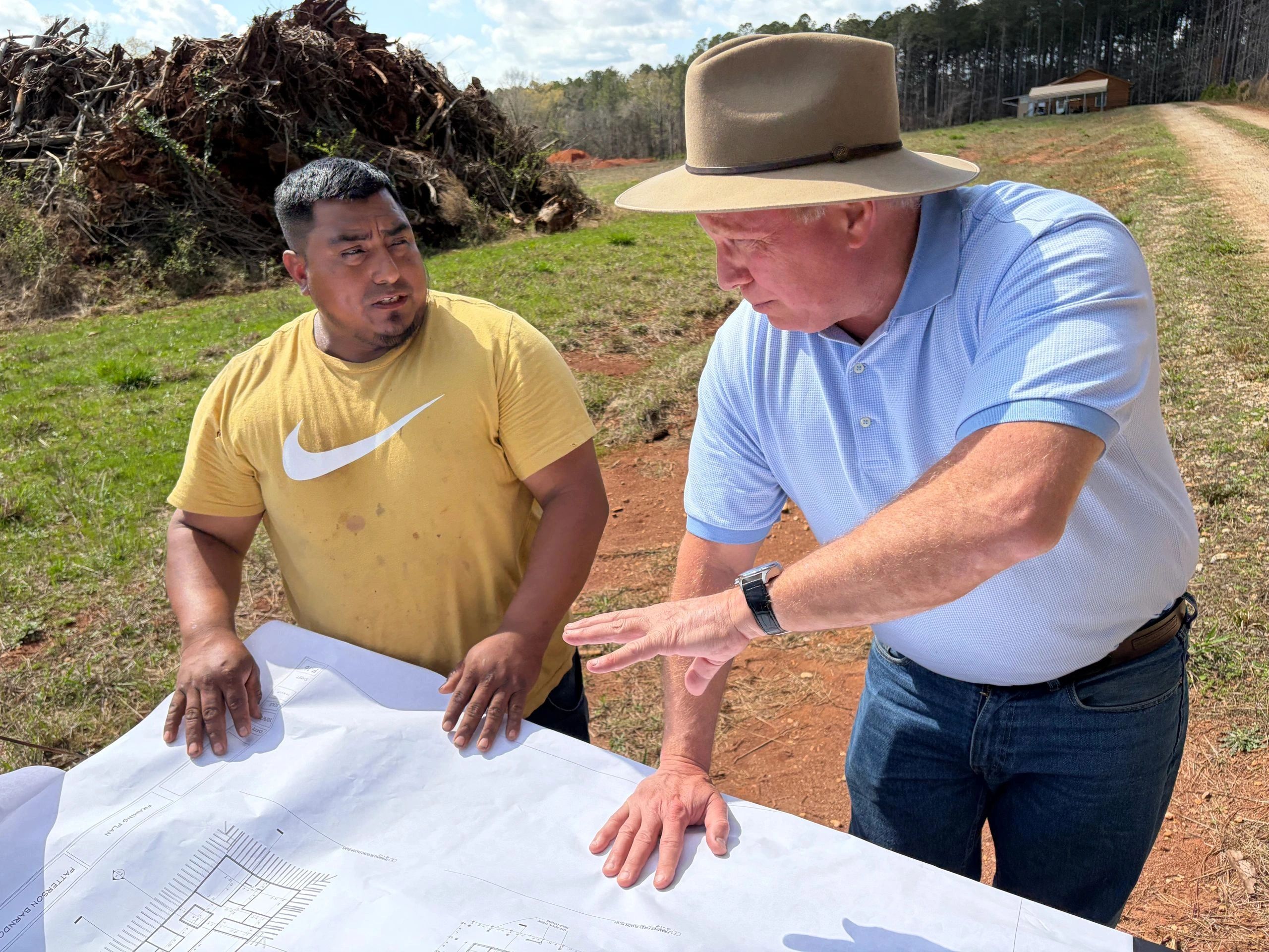 Two men examining blueprints outdoors on a sunny day.