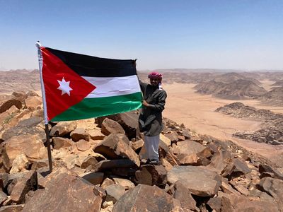 Man holding the Jordanian flag on a rocky mountain with desert landscape.