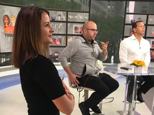 Woman standing next two two men sitting at a table on the live set of the TODAY show