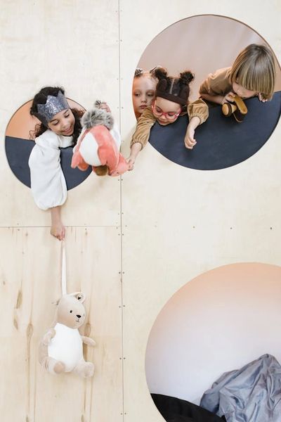 Children playing and sharing toys through circular openings in a wooden wall.